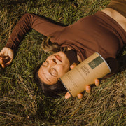 Woman in a brown top lying on a field and holding Your Super Super Green mix